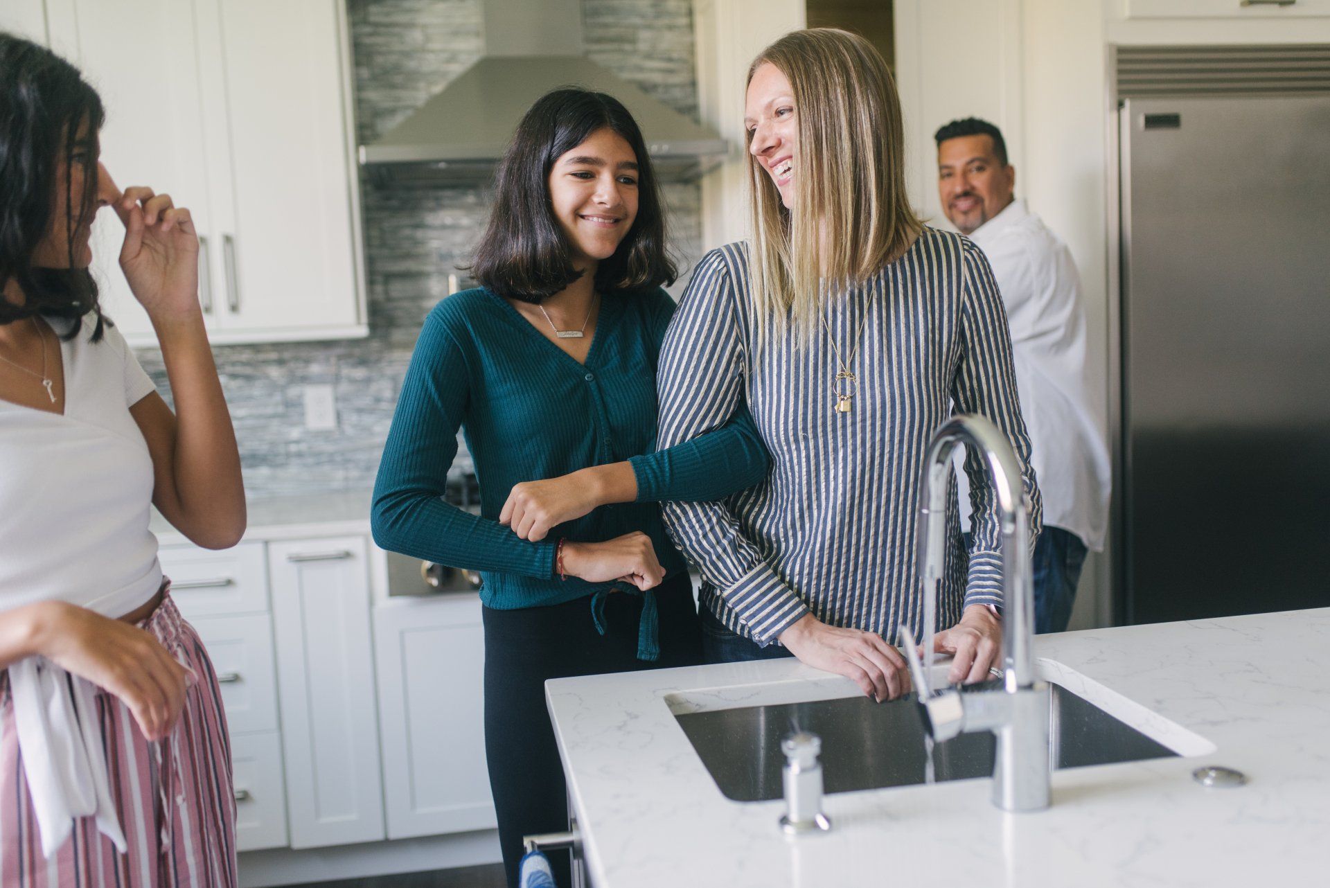 A family is standing in a kitchen near a sink.