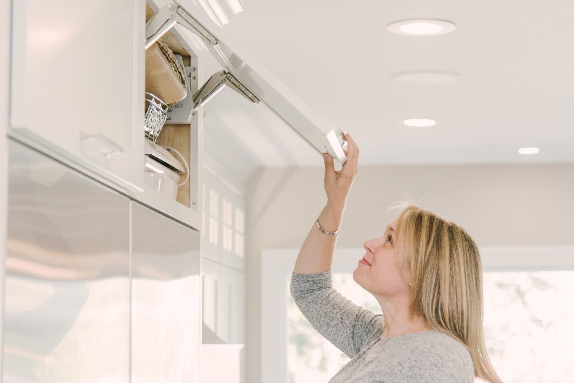 A woman is opening a cabinet door in a kitchen.