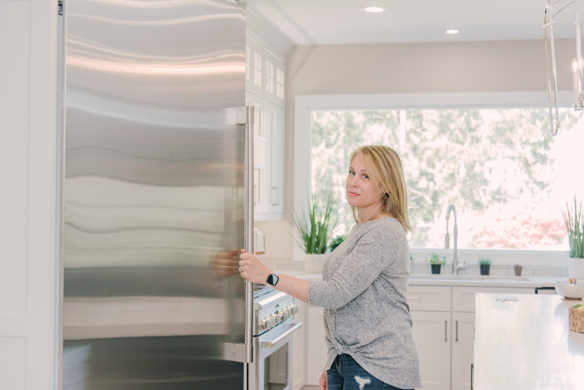 A woman is opening a stainless steel refrigerator door in a kitchen.