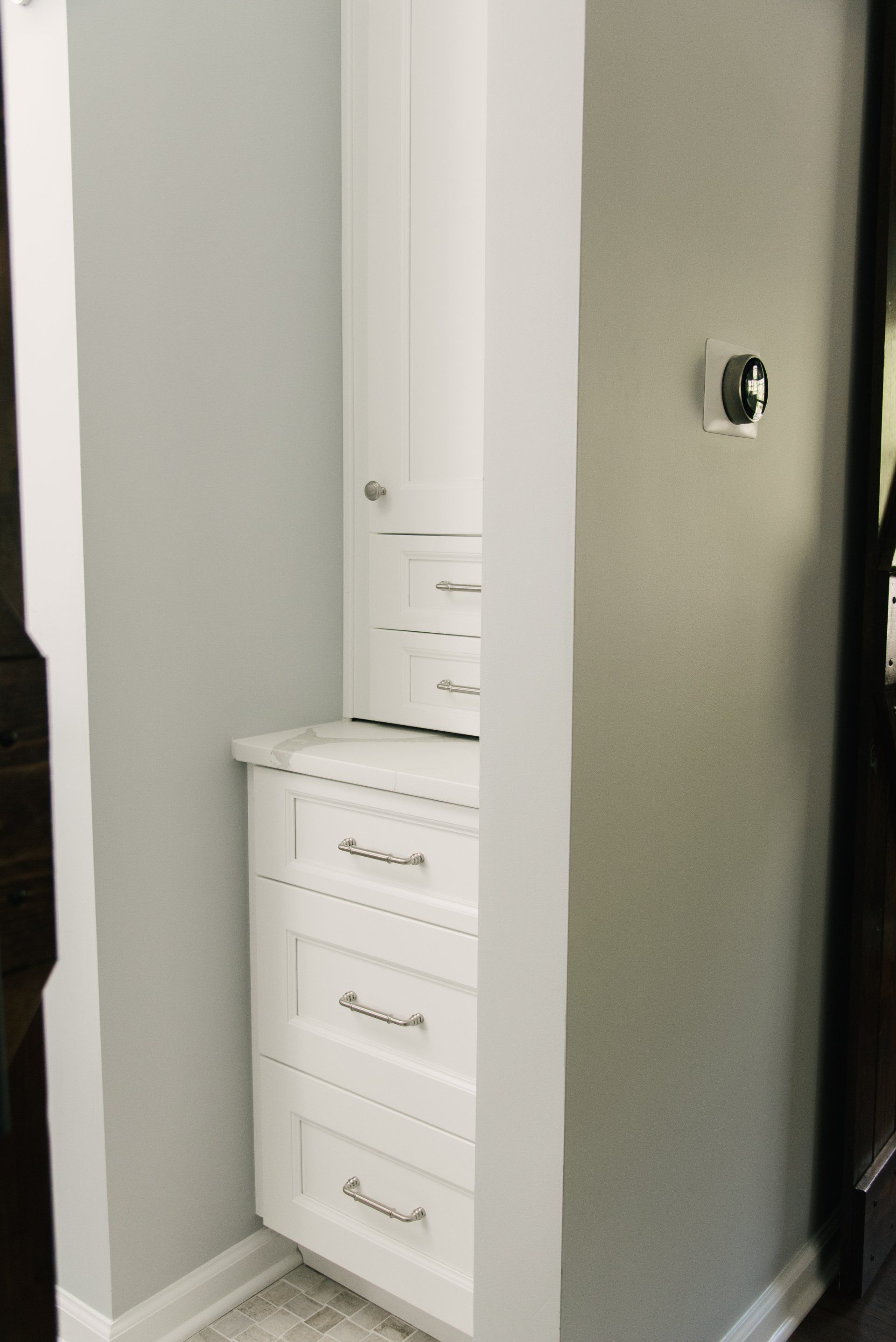 A bathroom with white cabinets and drawers and a thermostat on the wall.