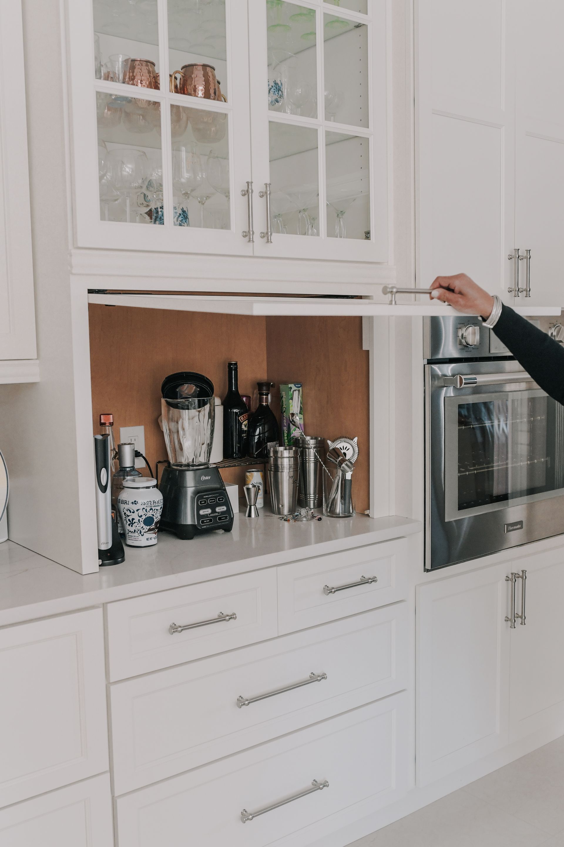 A person is opening a cabinet in a kitchen with a blender in it