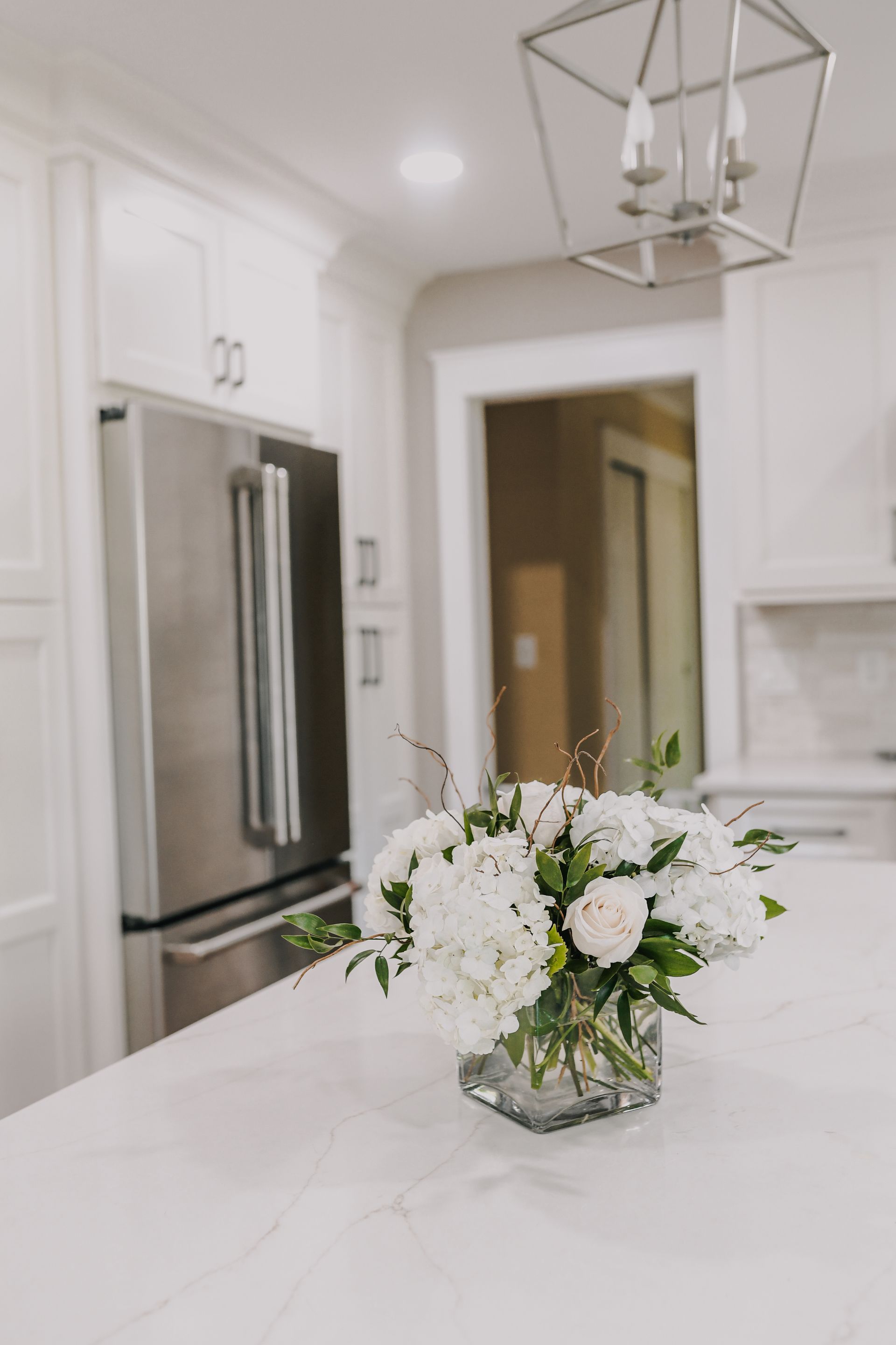 There is a vase of flowers on the counter in the kitchen.