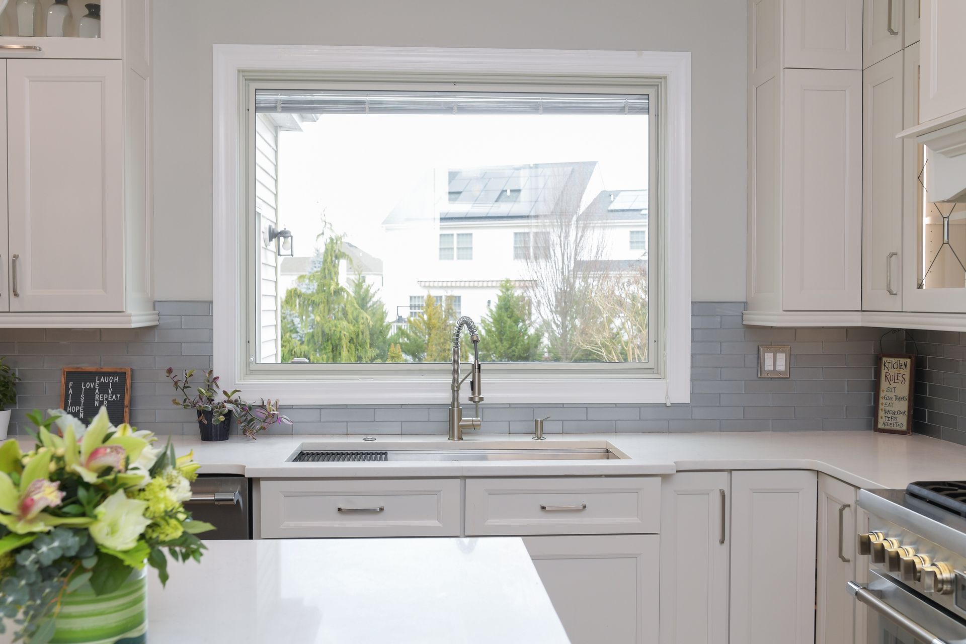 A kitchen with white cabinets , a sink , and a large window.