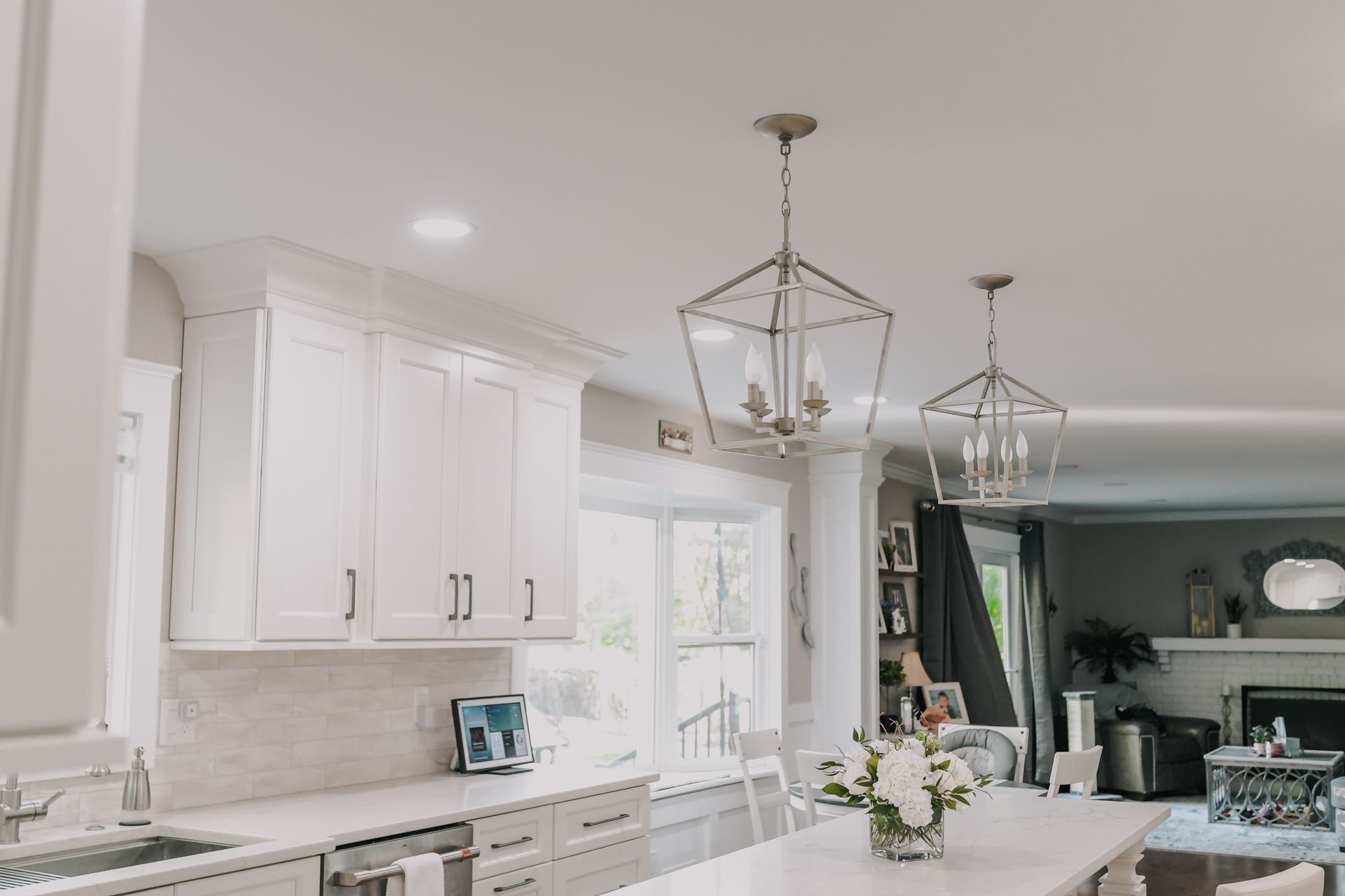 A kitchen with white cabinets , a large island , a sink , and a vase of flowers on the counter.