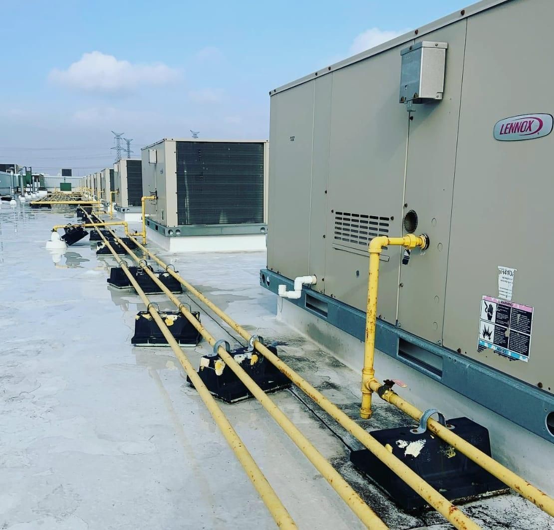 Rooftop HVAC units and yellow pipes along a flat roof under a blue sky