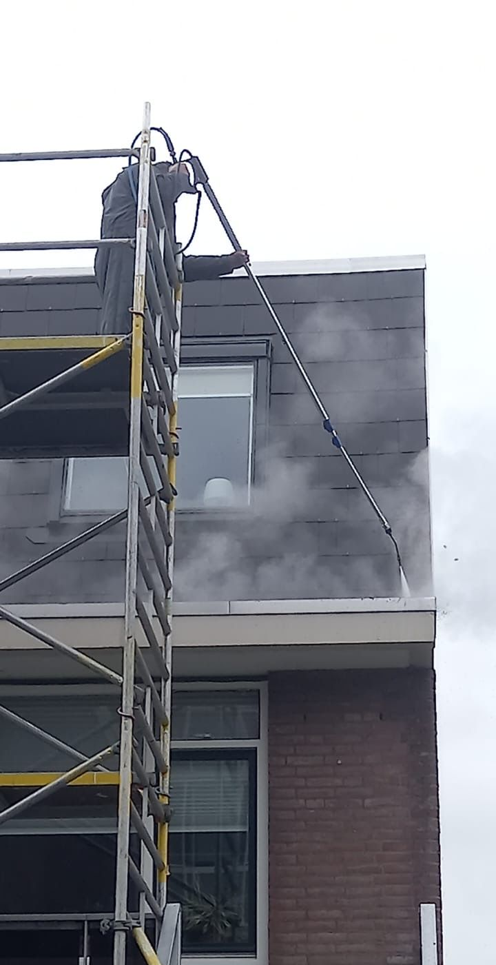 Mankracht wast de donkere buitenkant van een gebouw vanaf een steiger. Grijze mist verhult een deel van het gebouw.