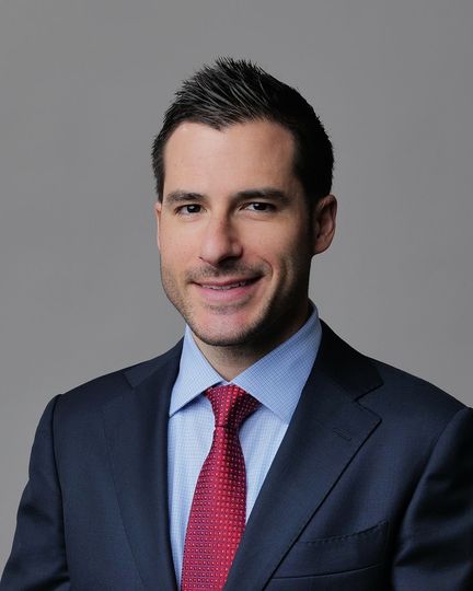 Man in a suit and tie smiling, set in a blurred medical office.