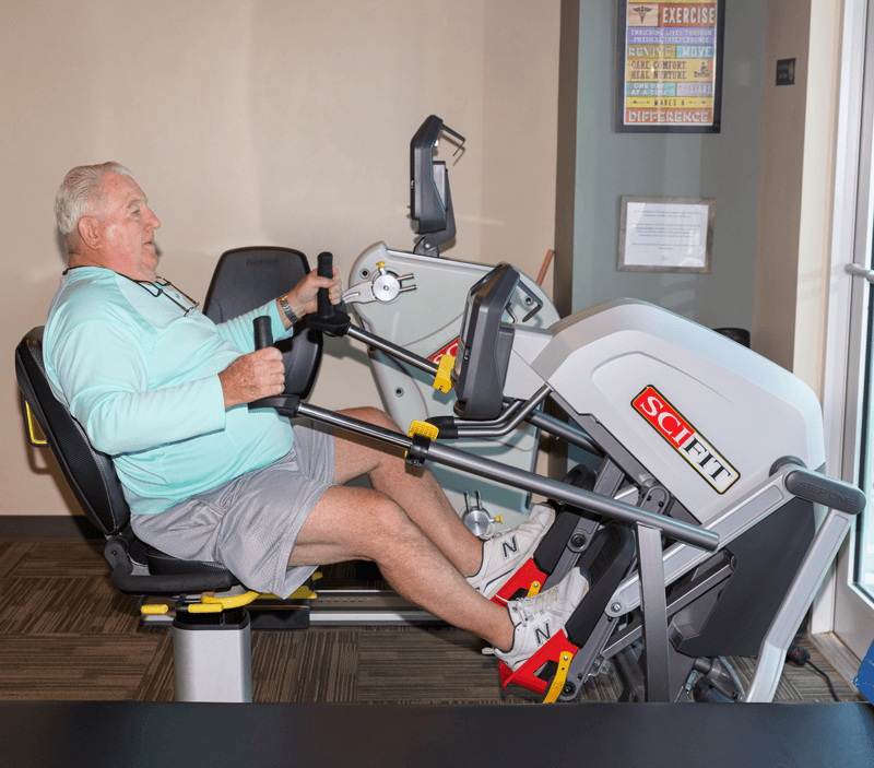 Man using SciFit exercise machine, pulling on handles and pushing pedals in gym setting.