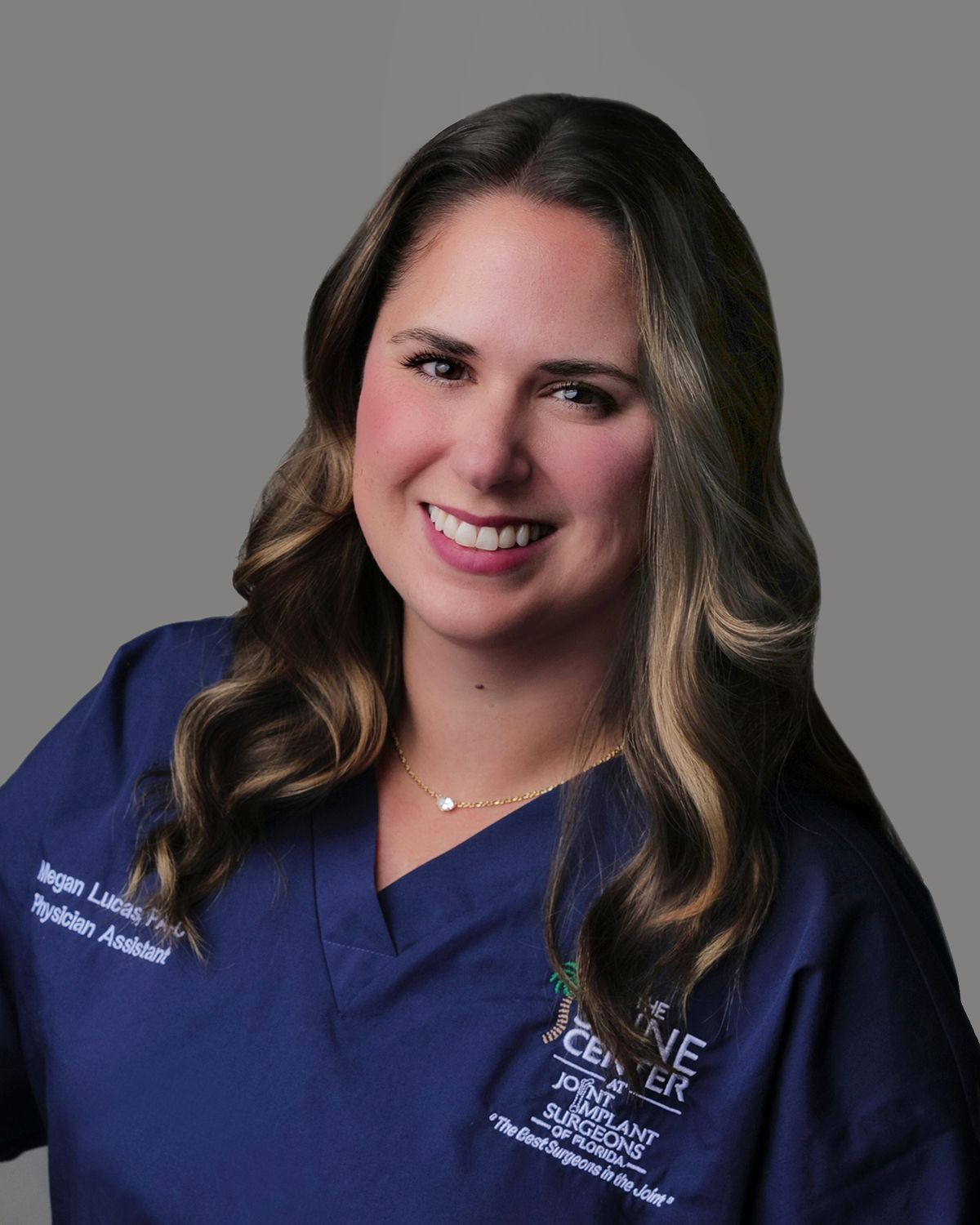 Woman with long brown hair smiles at the camera, wearing a black shirt with a medical setting backdrop.