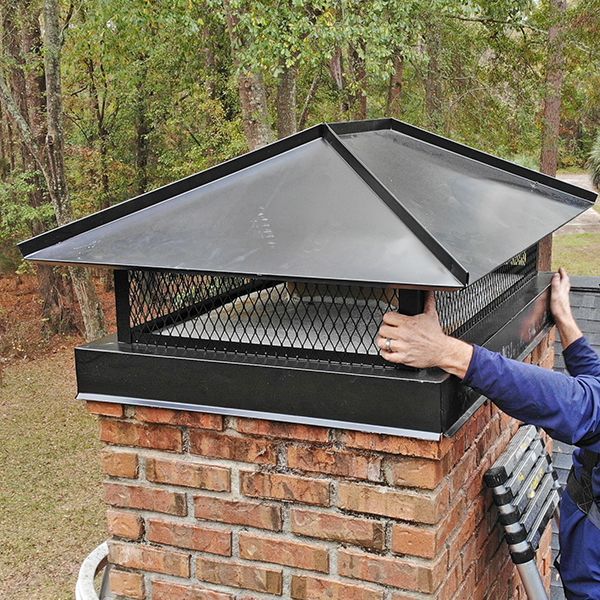 Person installing a black metal chimney cap on a brick chimney outdoors