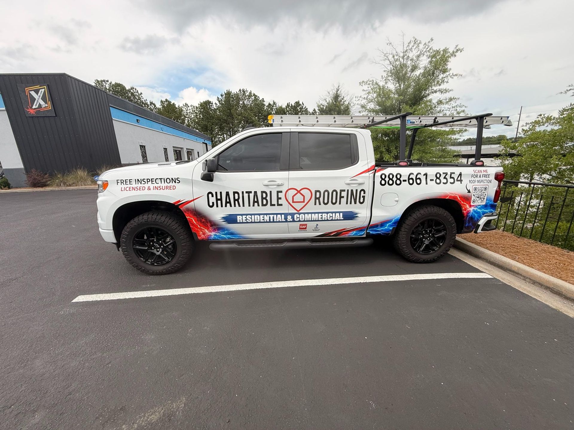 Charitable Roofing branded pickup truck parked in a lot near a building and chain-link fence.