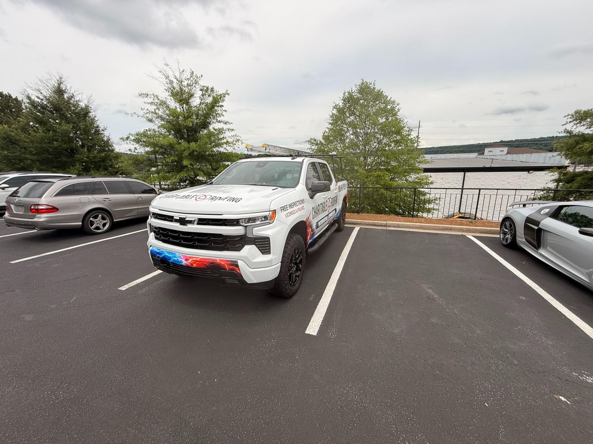 White pickup truck with red and blue front bumper parked in a lot near water, flanked by other cars.