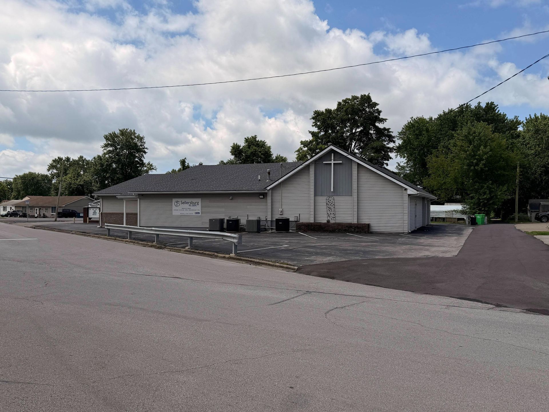 Low gray building with dark roof beside an empty paved lot under a cloudy sky
