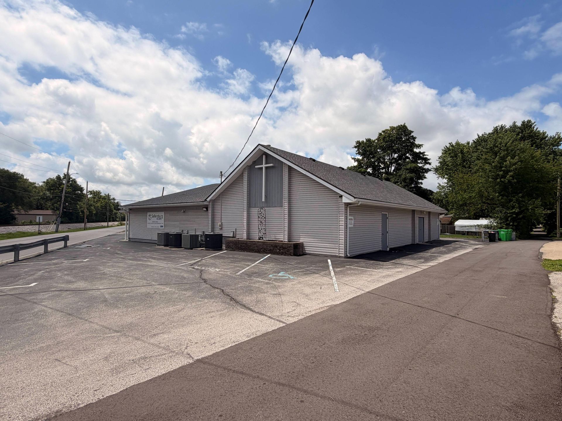 Gray industrial building with a sloped roof beside an empty paved lot under a cloudy sky