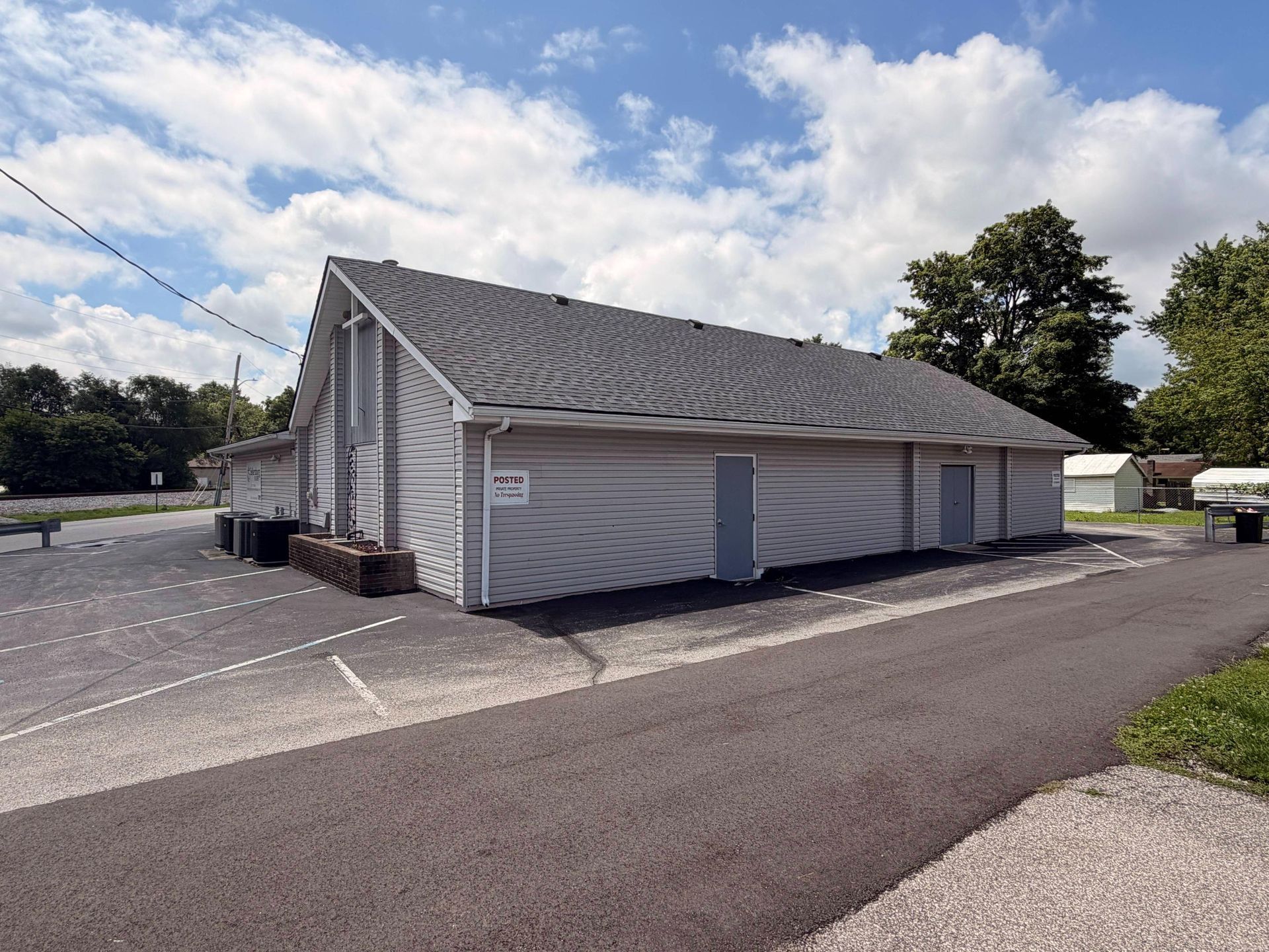 Small white building with gray roof beside a paved lot under a cloudy sky