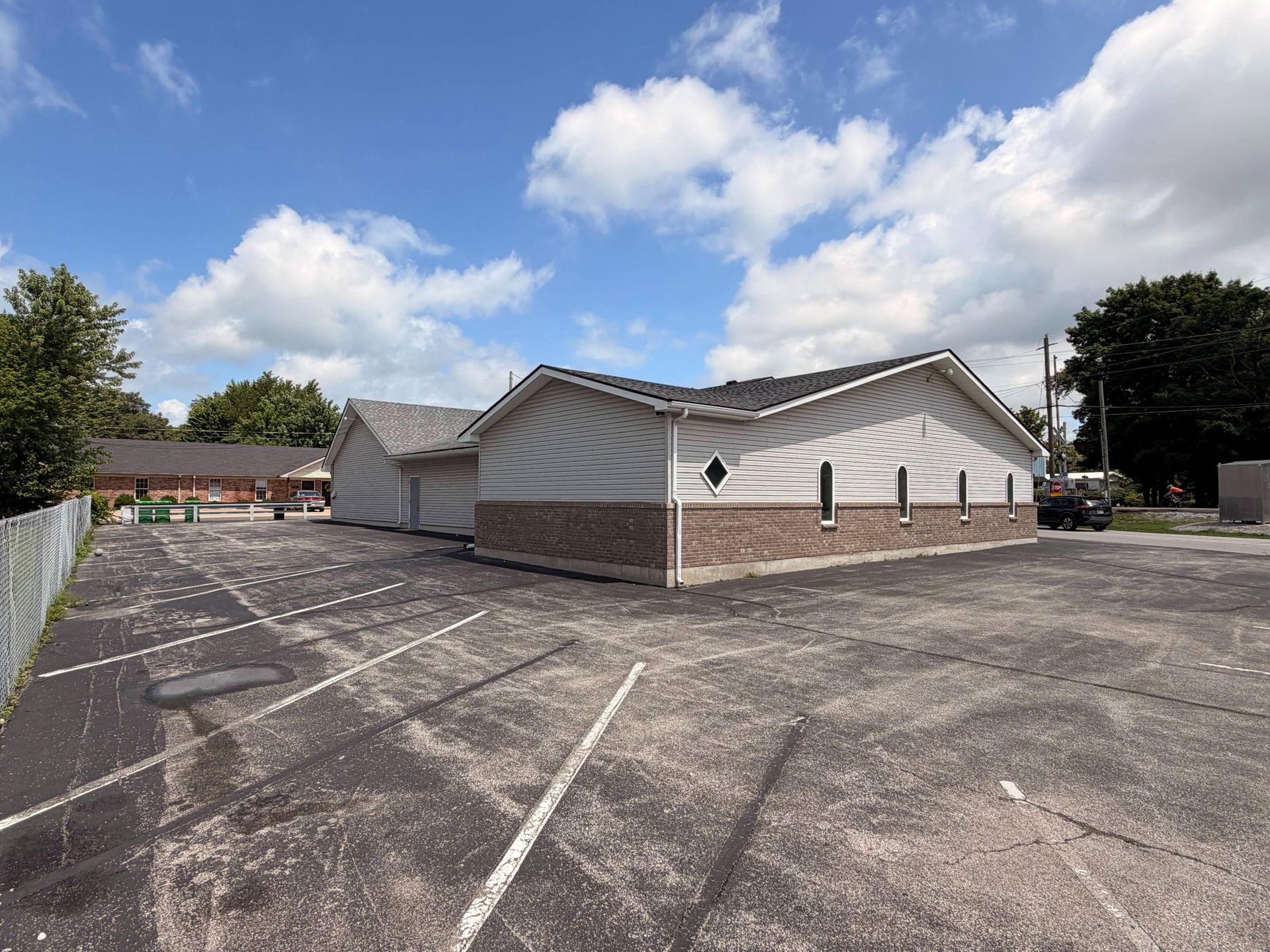 Empty parking lot beside a white building with a brick base under a blue, partly cloudy sky