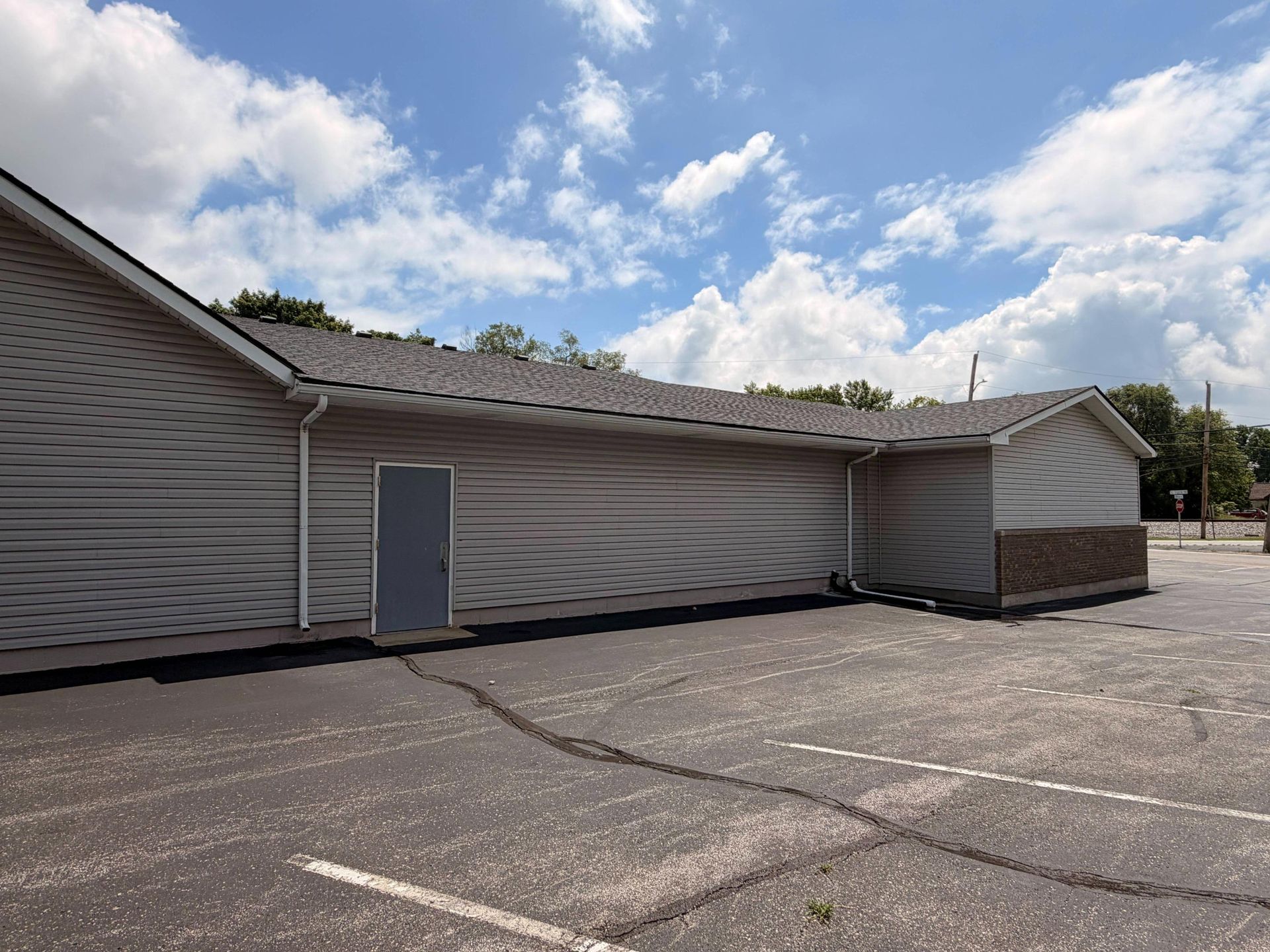 Single-story beige building with closed garage doors and a paved parking lot under a cloudy blue sky