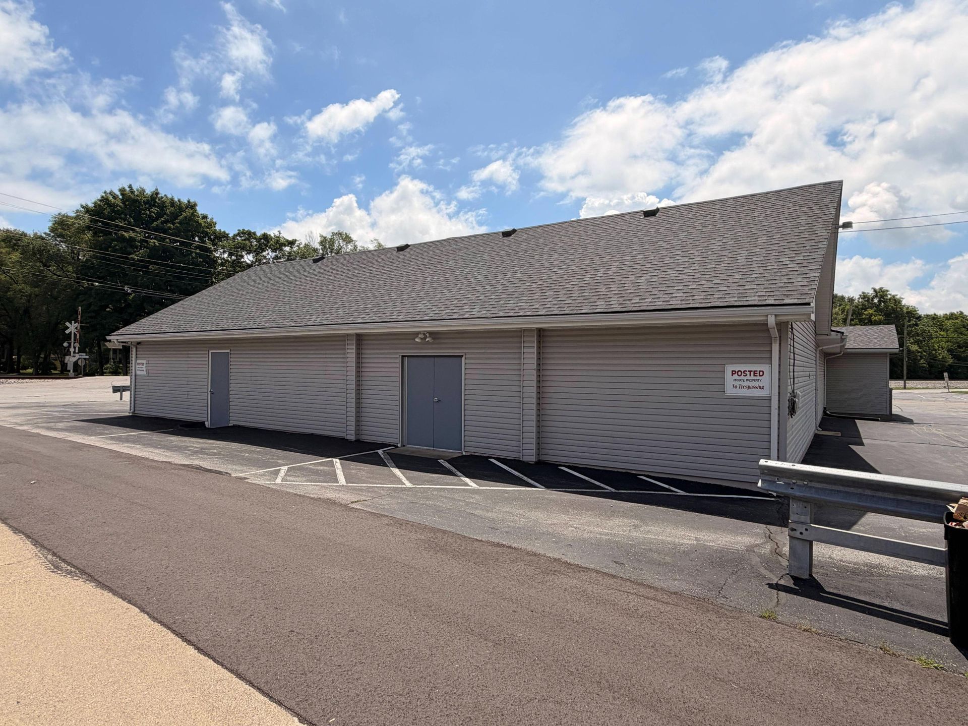 Single-story white building with a gray roof beside a paved road under a partly cloudy sky