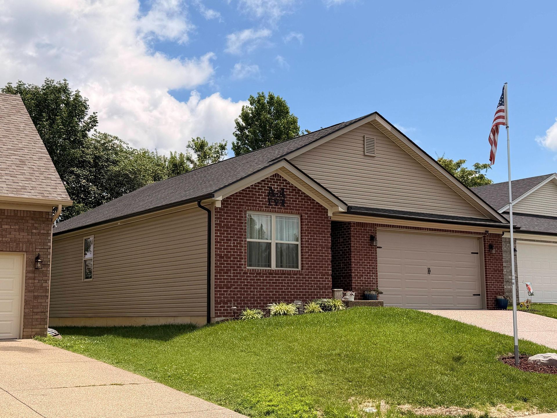Single-story brick and tan suburban house with garage, green lawn, and an American flag on a pole