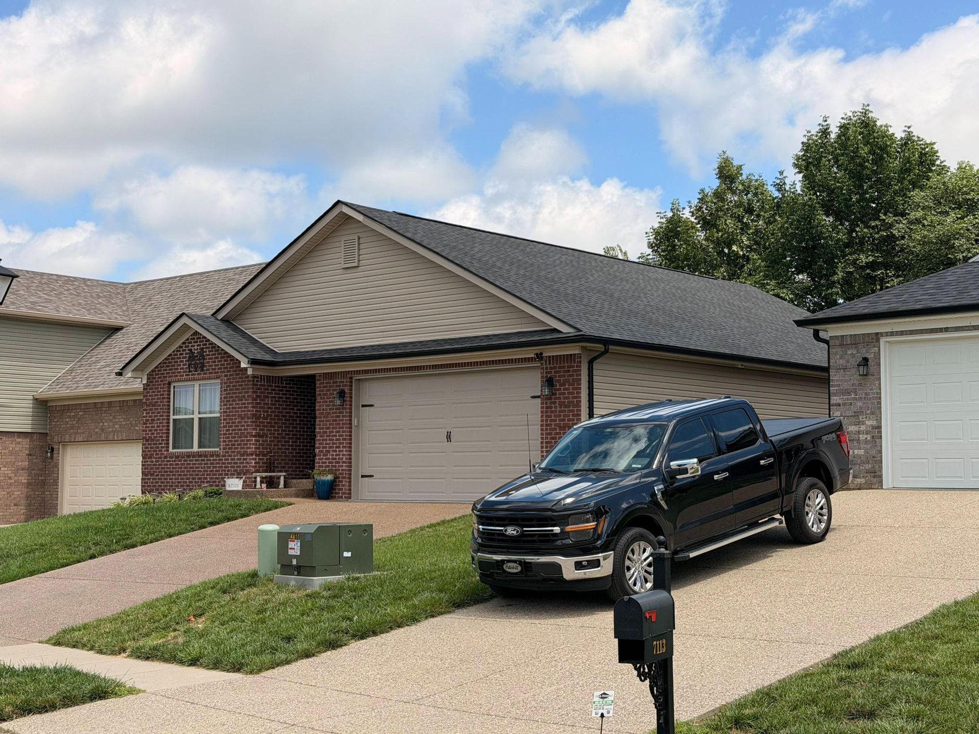 Black pickup truck parked in a suburban driveway beside a beige garage on a cloudy day