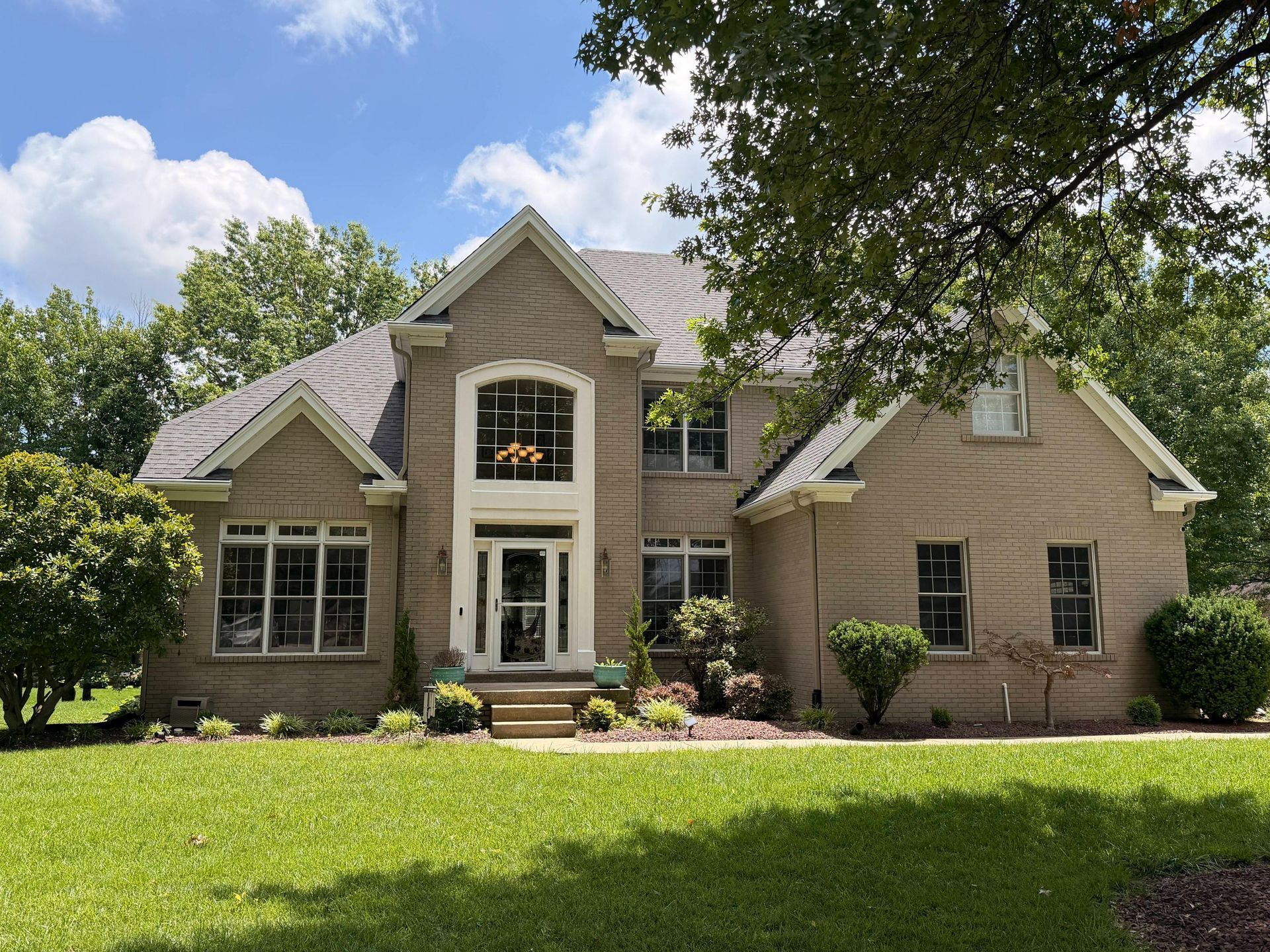 Suburban brick house with a gabled roof, large front windows, and a green lawn under a cloudy sky