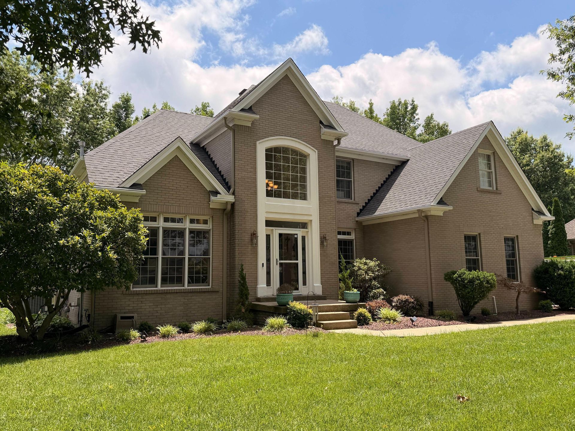 Suburban house with stone facade, large windows, and a manicured green lawn under a blue sky