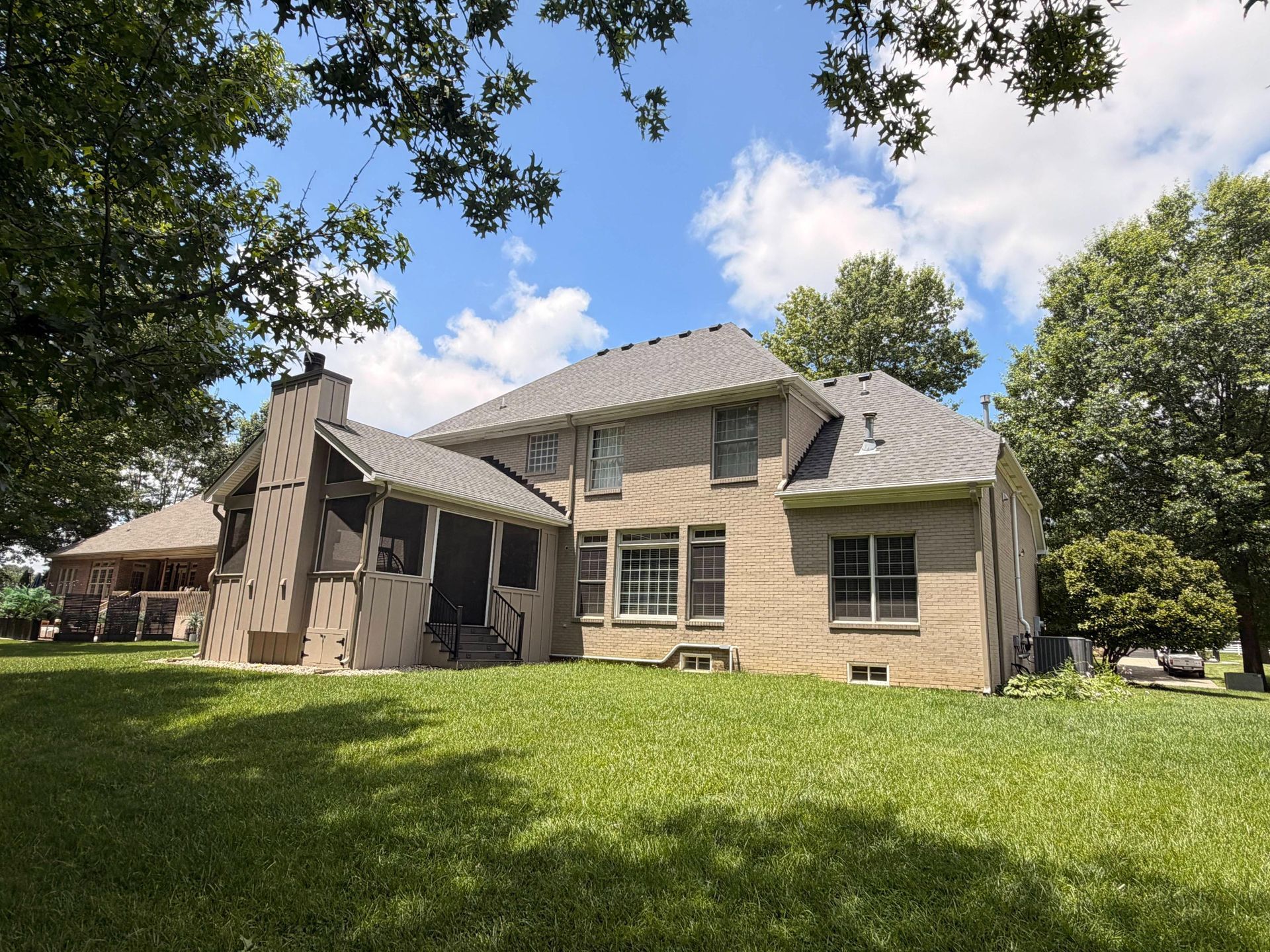 Stone house with a gabled roof and green lawn under a partly cloudy sky, framed by trees