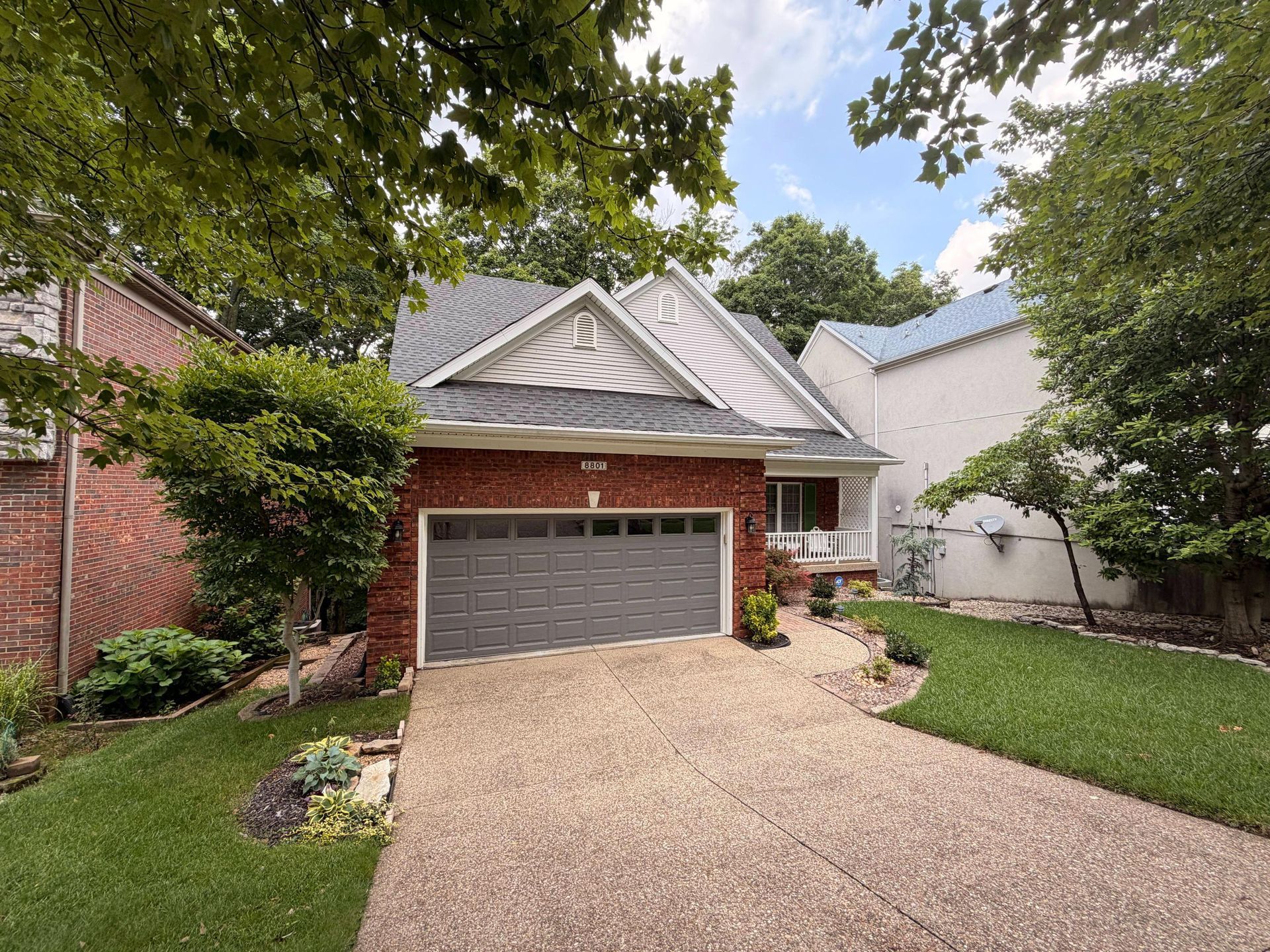 Suburban house with a gray garage, brick facade, and tree-lined driveway