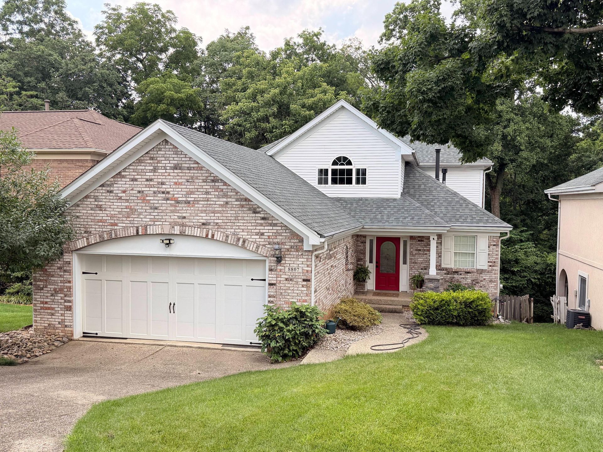 Suburban two-story house with stone facade, white garage, red front door, and green lawn