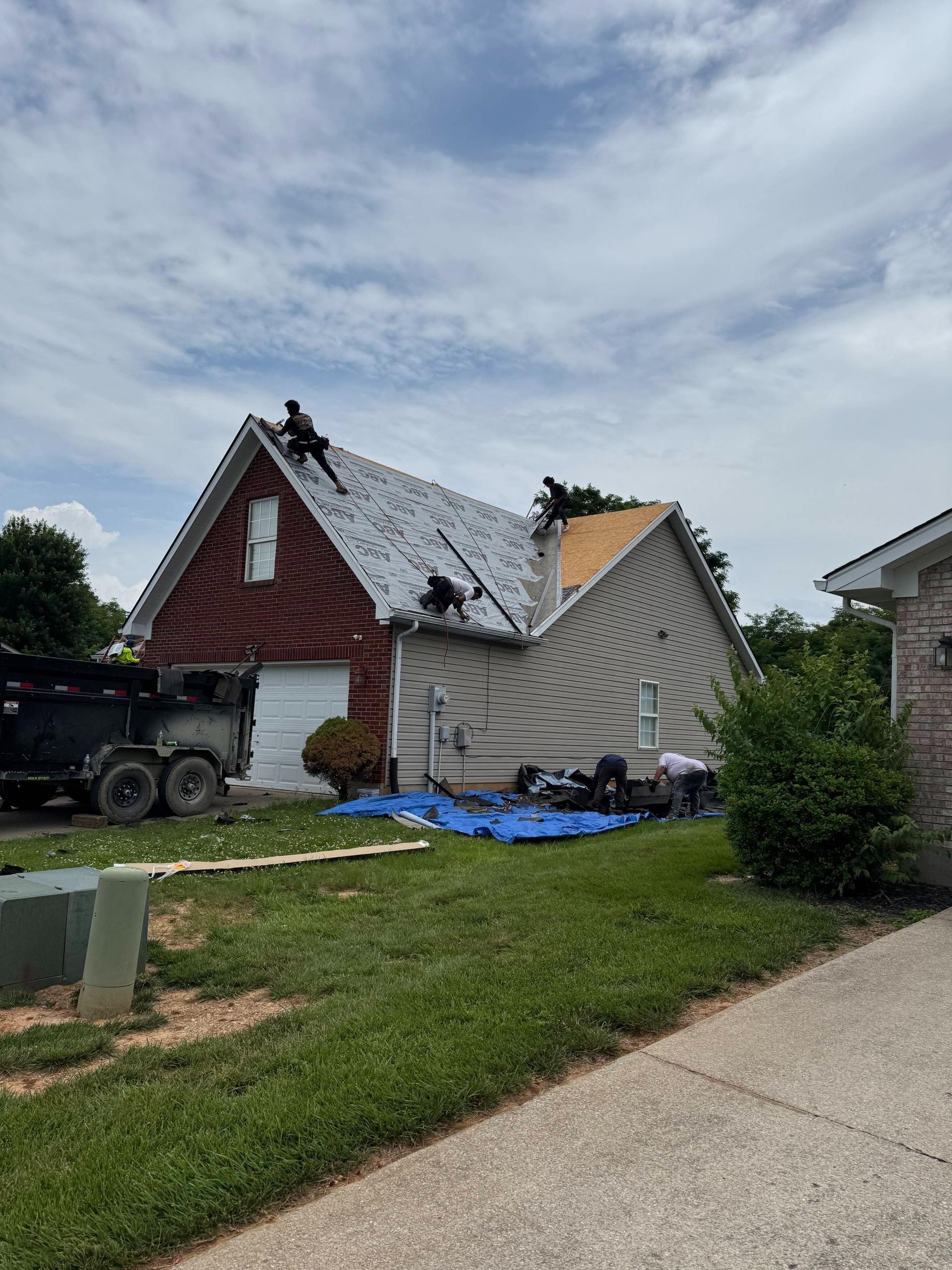Damaged house with a collapsed roof, debris in the yard, and a blue tarp after a storm