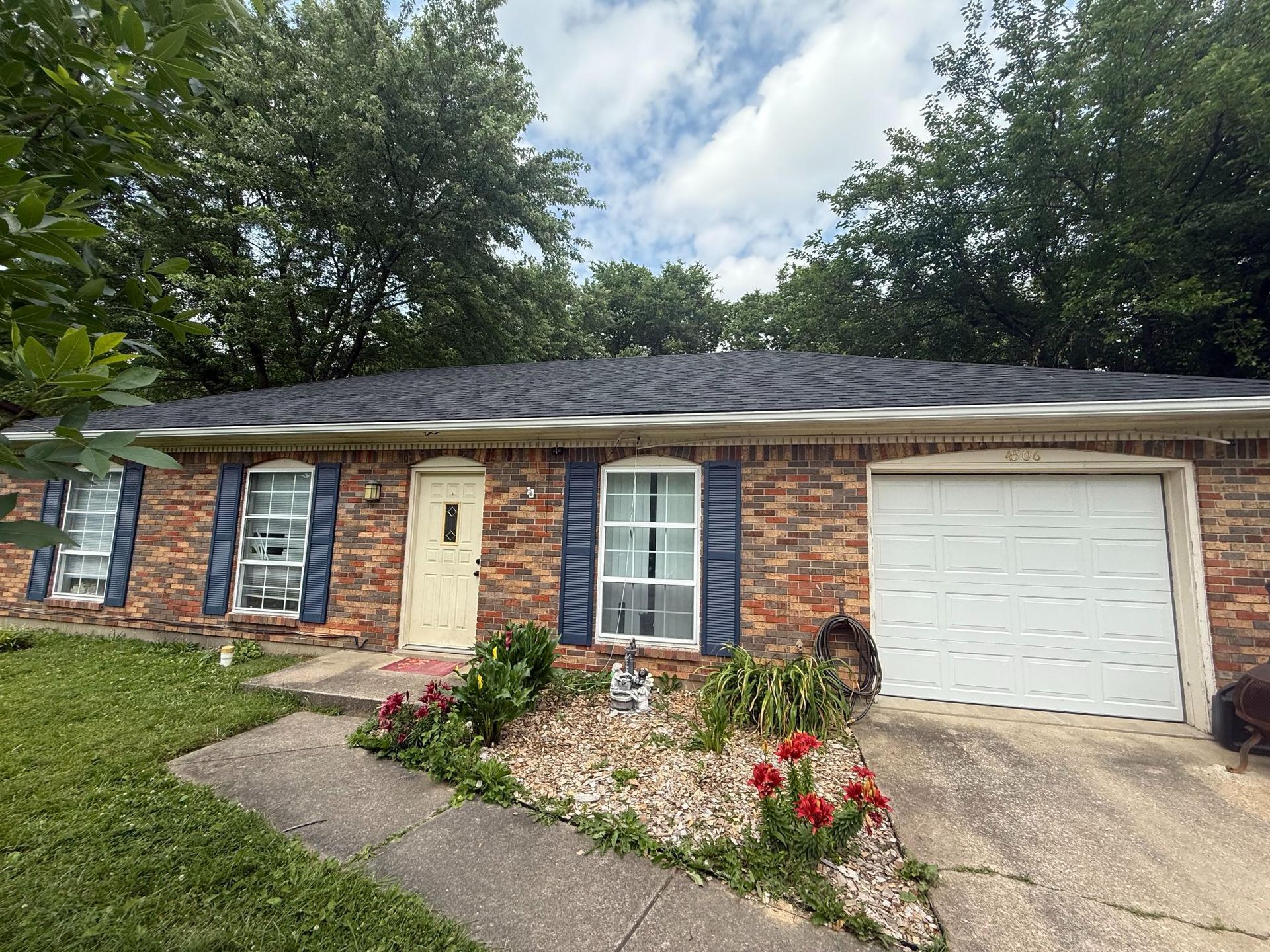 Single-story brick house with a white garage door, front porch, and flower garden by a concrete walkway