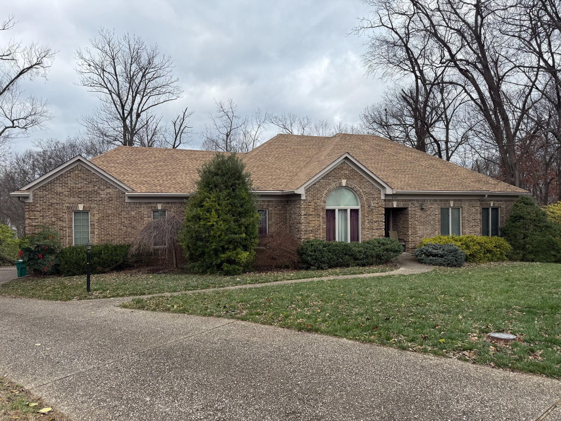 Single-story brick house with tan roof, driveway, and leafless trees in front yard