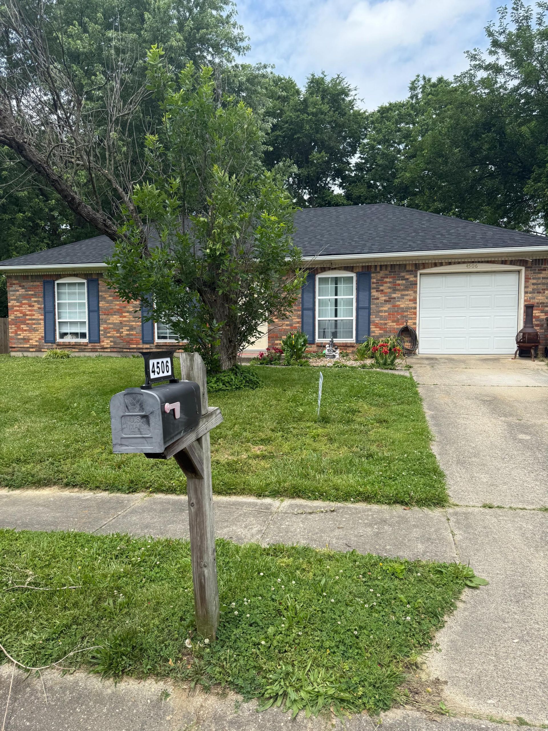 Suburban brick house with a front lawn, driveway, and mailbox by the sidewalk.