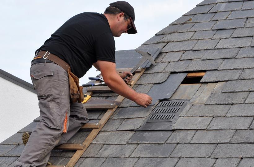 Worker installing shingles on a roof with a hammer and ladder access