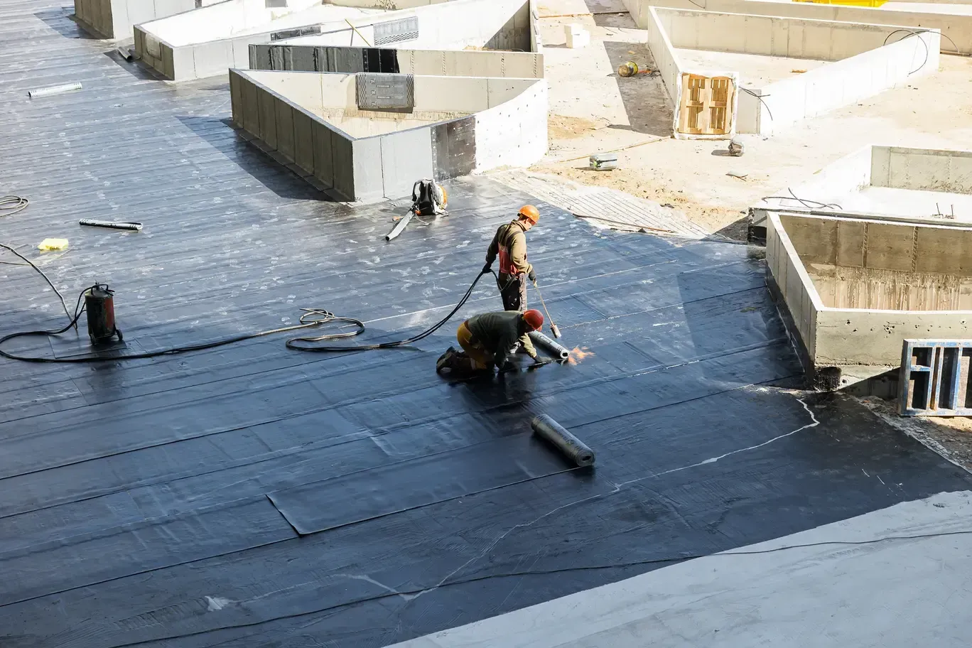 Worker on a roof repairing purple flashing beside brown tiles under a clear blue sky