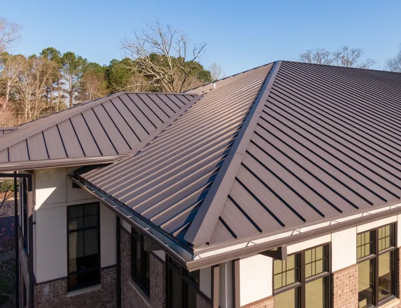 Aerial view of a modern house with a dark metal roof and large windows in a wooded setting