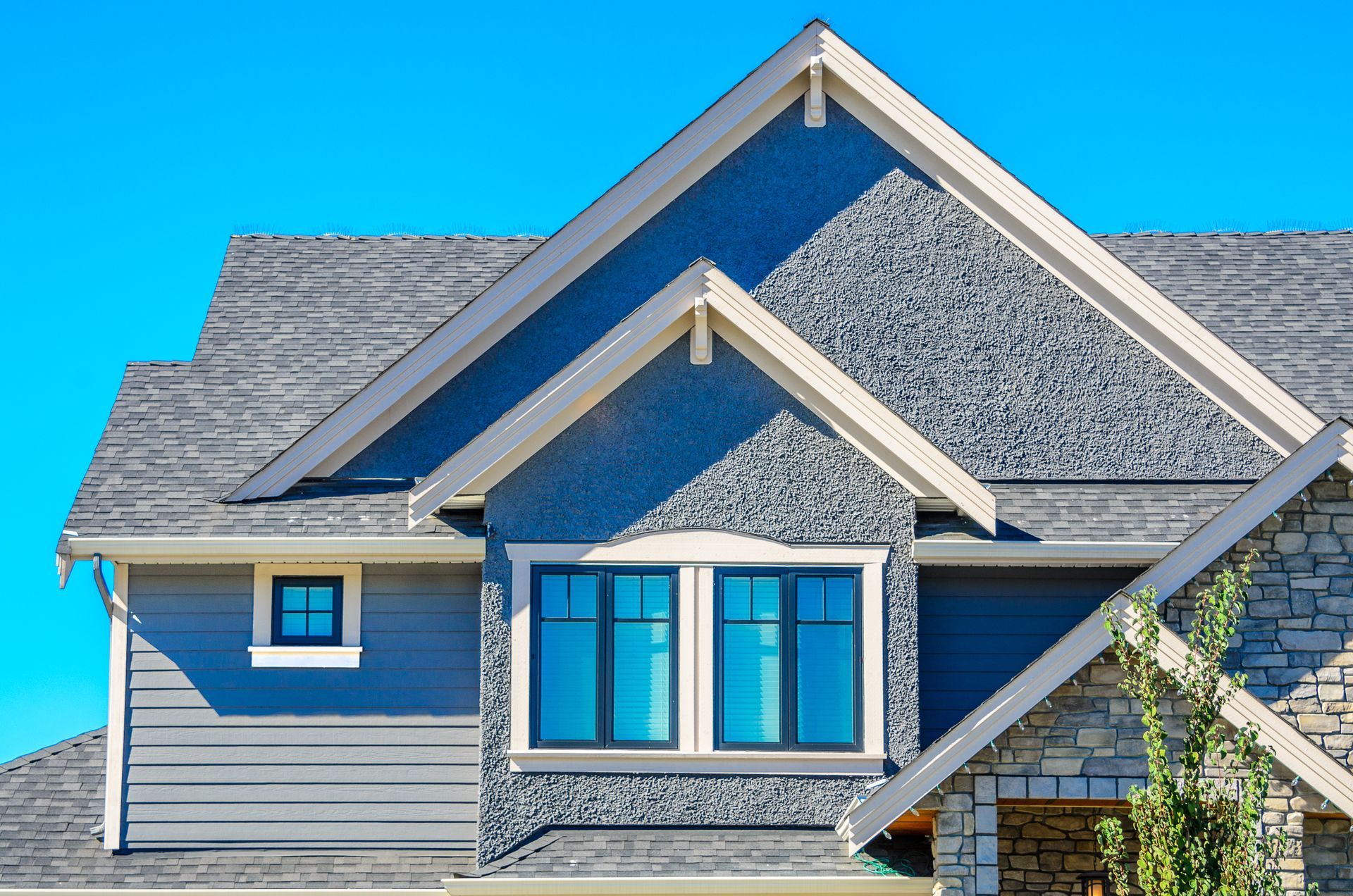 Gray house roof and blue-trimmed windows under a bright blue sky