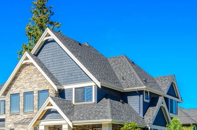 Stone-and-blue siding house with steep gabled roof against a clear blue sky