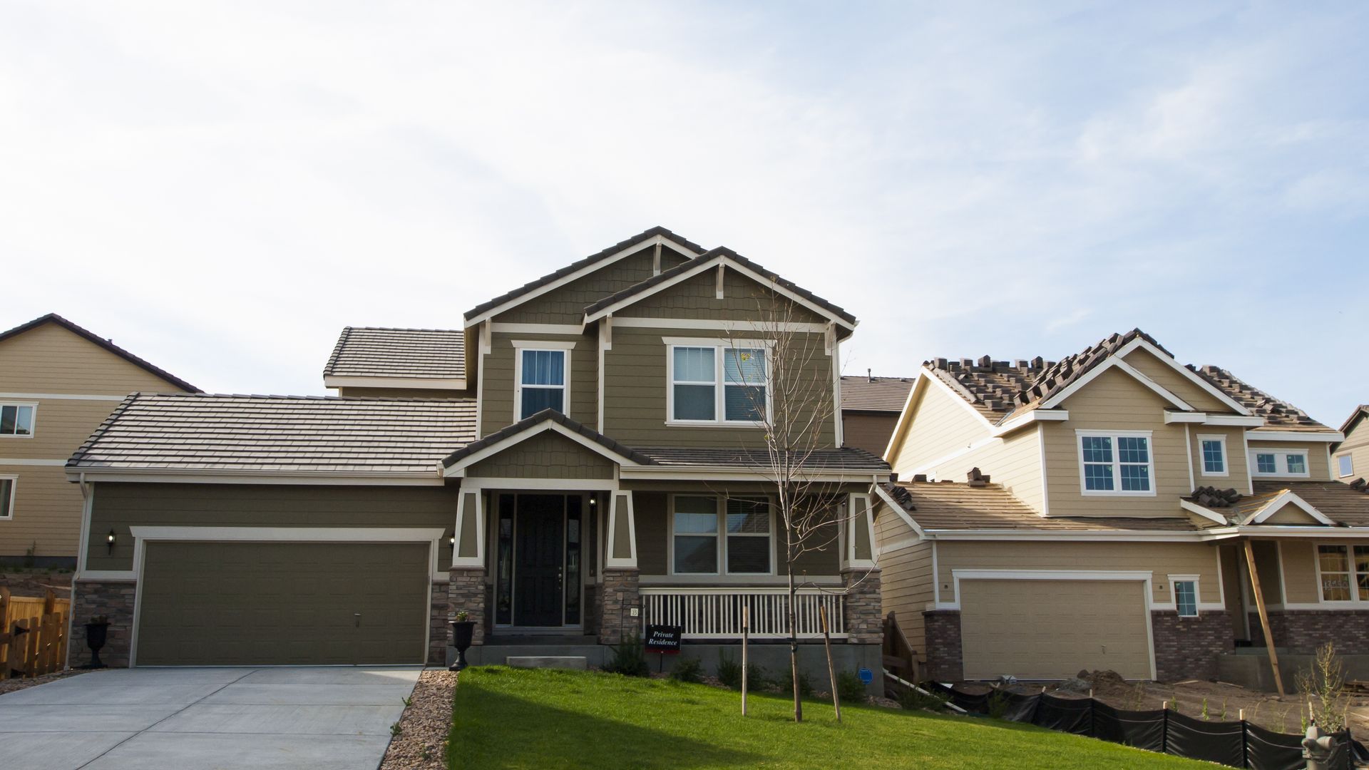 Suburban two-story house with beige siding, a front porch, and an attached garage under a cloudy sky