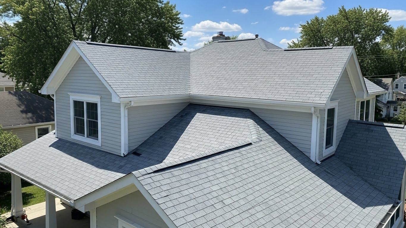 Gray shingled house roof with dormers and white trim, seen from above on a sunny day