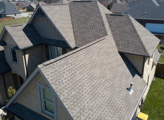 Aerial view of a house roof with gray shingles and multiple gables in a suburban neighborhood