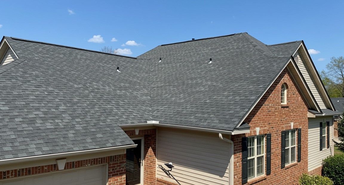 Brick house with dark gray shingled roof under a blue sky