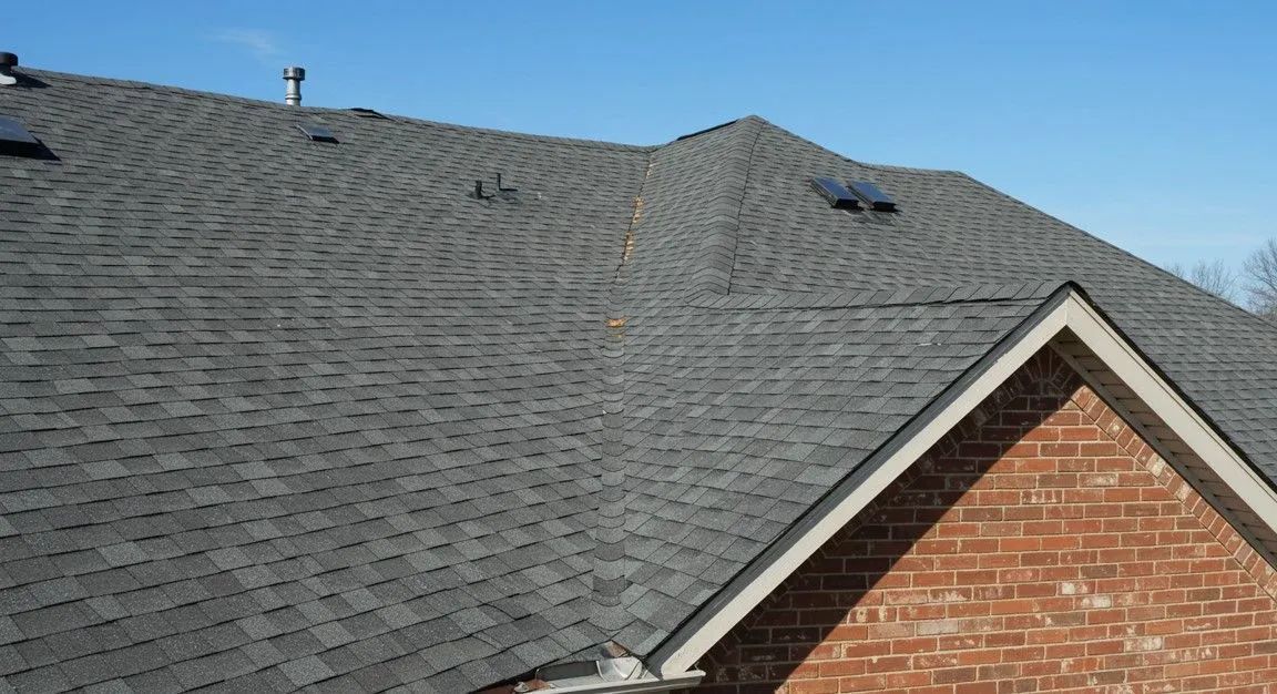 Gray shingled roof with a brick gable against a blue sky