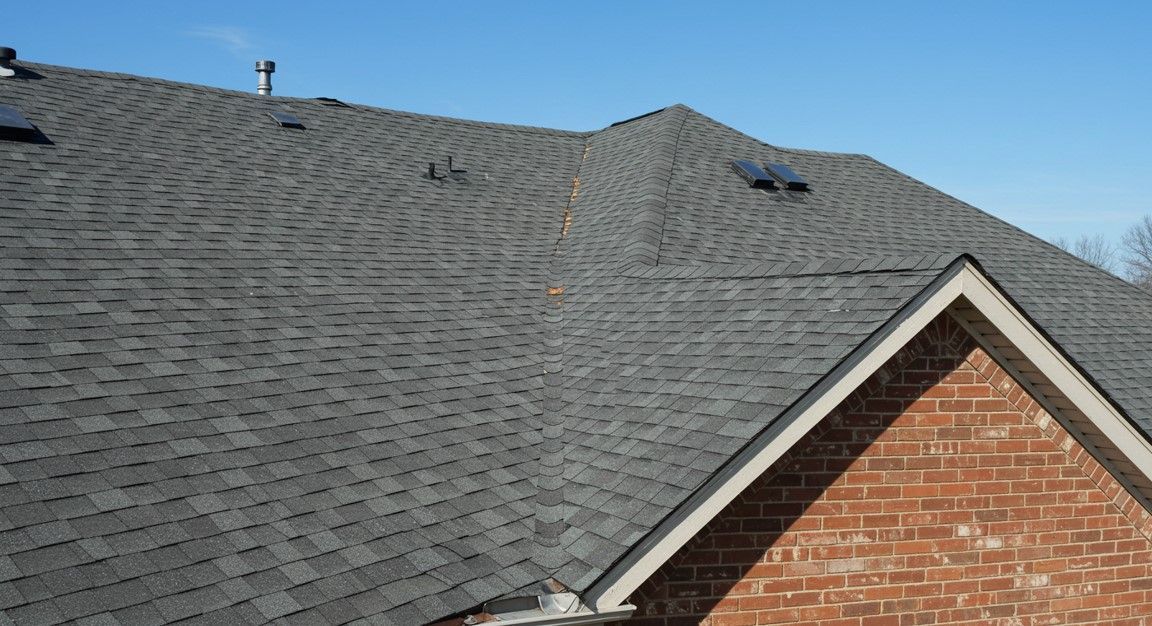 Gray shingle roof with visible damage near the ridge above a brick house gable