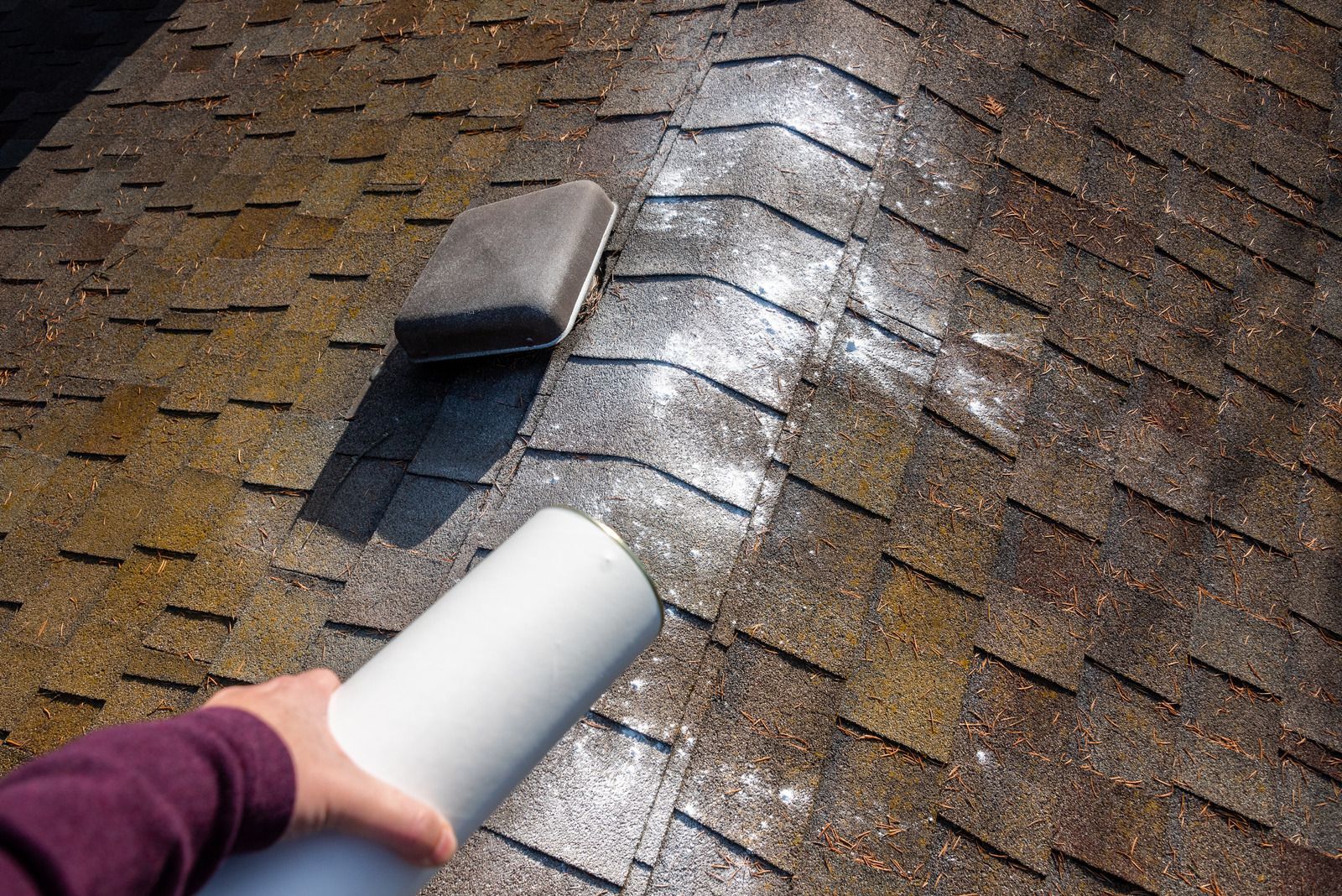 Hand holding a white roof vent or inspection tool over a shingled roof with a skylight window