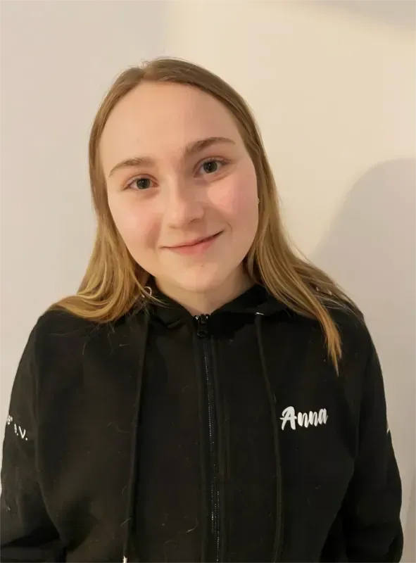Person in schwarzem Kapuzenpullover lächelt vor einer hellen, schlichten Wand