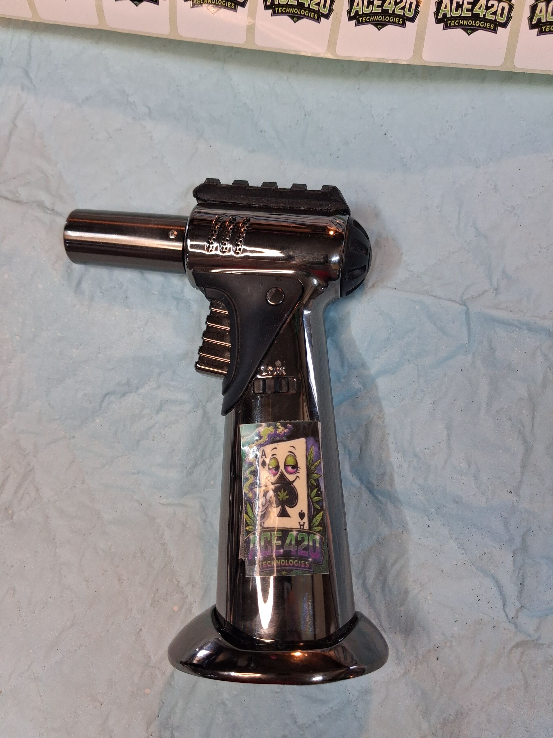 Black handheld butane torch on a light blue cloth background