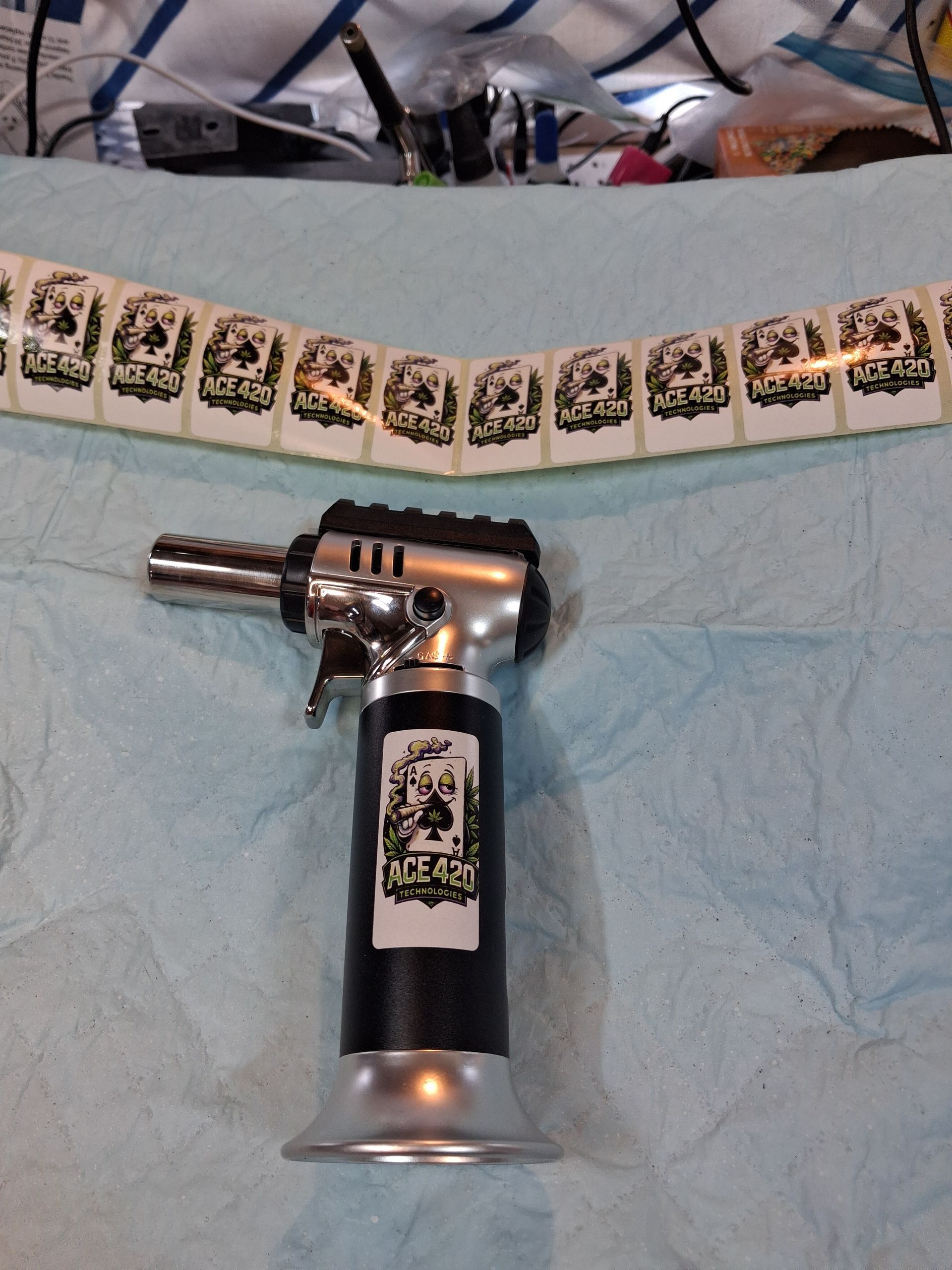 Metal torch lighter standing on a blue cloth with a row of stickers in the background.