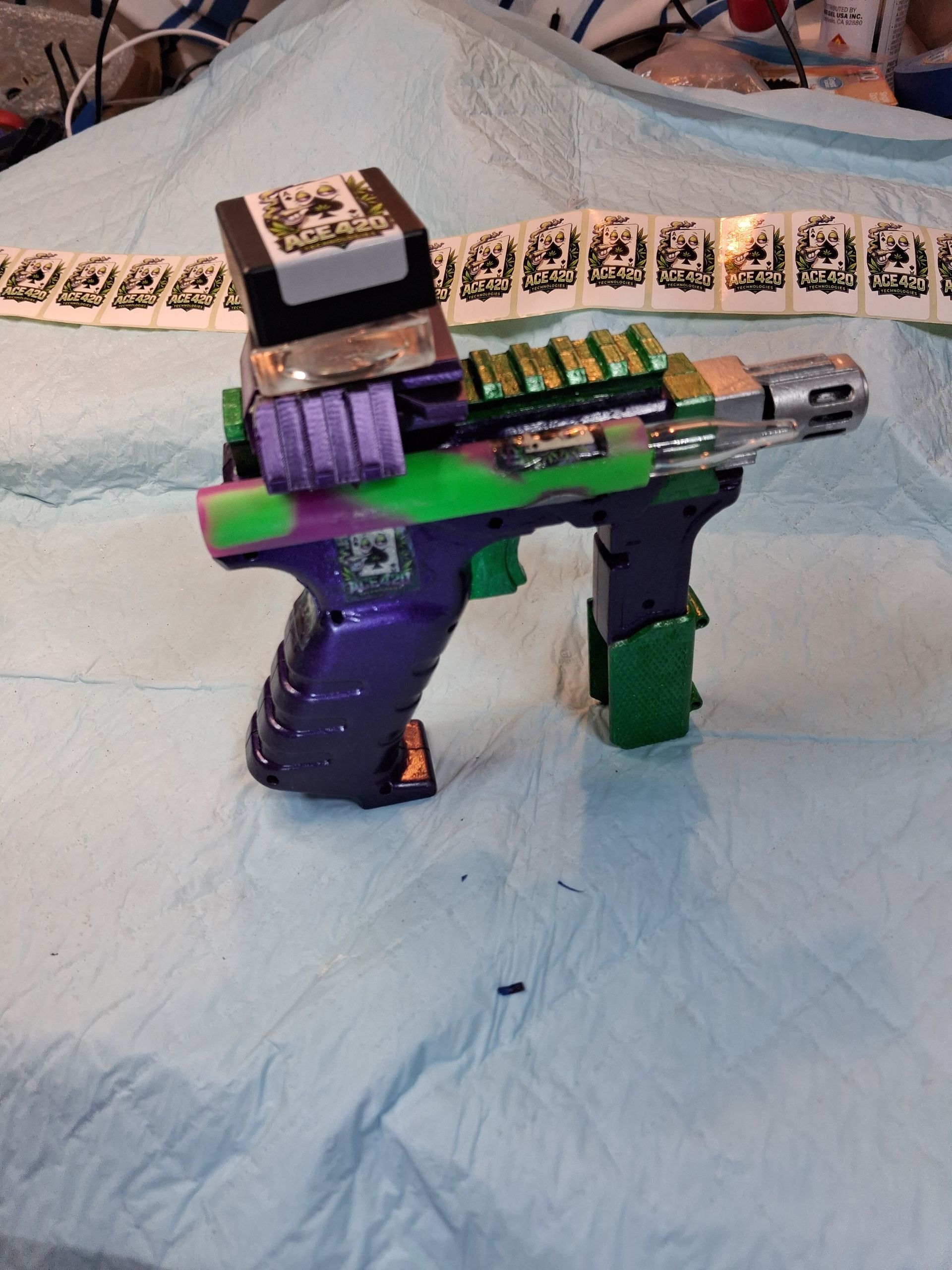 Purple-and-green toy gun with matching accessories laid on a light blue cloth.