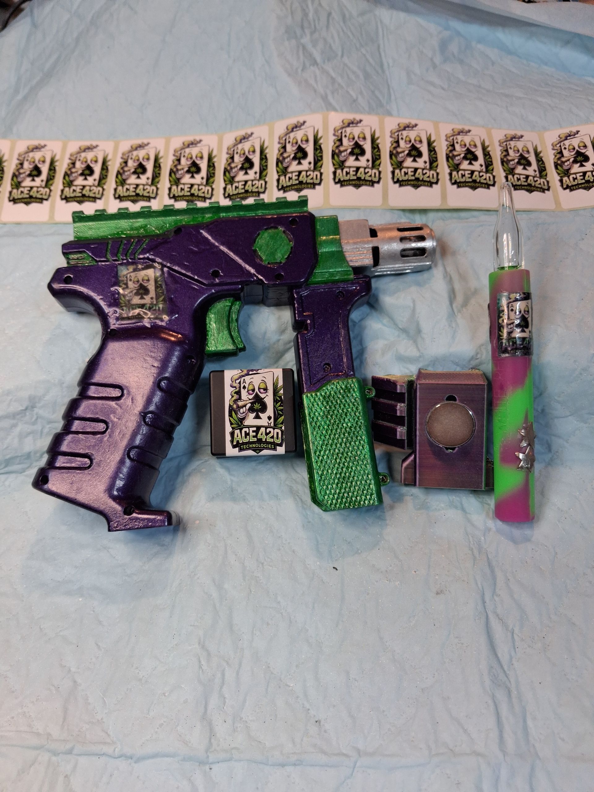 Purple-and-green toy gun with matching accessories laid on a light blue cloth.